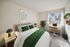 Cozy bedroom with a modern work desk by a bright window, lush greenery, and stylish decor.