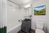 Modern bathroom featuring a sleek black vanity with a granite countertop, elegant bathtub with a white and green shower curtain, and a scenic landscape artwork on the wall.