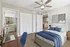 Charming bedroom with cozy bed, modern ceiling fan, and a workspace featuring a sleek laptop, leading to a stylish bathroom and open kitchen area.