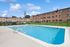 Charming apartment complex with a sparkling outdoor swimming pool, surrounded by lush greenery and spacious seating area under blue skies.