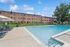 Inviting apartment complex with a sparkling community pool, surrounded by lounge chairs and lush greenery under a clear blue sky.