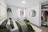Modern bedroom featuring a cozy bed with green accents, round wall mirror, and open closet offering ample storage space.