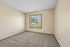 Bright and airy empty room featuring plush carpet and a large window with a serene view of lush greenery.