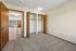 Bright bedroom with spacious closets, warm carpeting, and an inviting view into a sunlit living area with wooden accents.