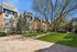 Charming apartment building surrounded by lush greenery and a well-maintained courtyard, featuring tall trees and a cozy pergola area.