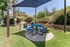 Inviting outdoor picnic area with a modern blue table set under a stylish shade canopy, surrounded by lush greenery and vibrant flowers.