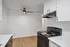 Contemporary kitchen with sleek black appliances, elegant white cabinetry, and stylish wood flooring, featuring a modern ceiling fan for a refreshing ambiance.