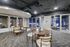 Elegant communal space with modern round tables and stylish chairs, featuring a sleek ceiling with subtle lighting accents and large glass doors, perfect for social gatherings or meetings.
