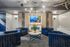 Modern lounge area with stylish blue velvet chairs, geometric decor, and a wall-mounted flat-screen TV, creating a cozy and inviting atmosphere.