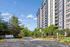 Modern high-rise apartment building with lush landscaping and clear blue skies, featuring contemporary design and ample greenery.