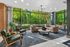 Elegant living room with plush beige sectional, stylish armchairs, and expansive floor-to-ceiling windows offering a lush green view.