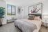 Bright and inviting bedroom with modern decor, featuring a cozy bed, stylish artwork, and a large window offering stunning cityscape views.