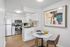 Modern kitchen with sleek white cabinetry, stainless steel appliances, and a cozy dining nook boasting contemporary artwork.