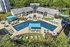 Luxurious outdoor pool area surrounded by modern lounge chairs and shaded seating, set against a scenic backdrop of greenery and elegant architecture.