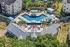 Aerial view of luxurious apartment complex featuring a stunning geometric pool, ample seating with umbrellas, and lush landscaping for a serene atmosphere.