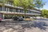 Modern apartment building with a shaded parking area surrounded by lush green trees, offering a serene and convenient living environment.