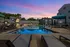 Charming poolside view at sunset with modern apartments, cozy lounge chairs, and vibrant blue umbrellas.