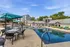 Elegant apartment complex featuring a pristine swimming pool with shaded lounge areas, surrounded by modern architecture and lush greenery.