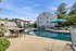Inviting apartment complex featuring a sparkling outdoor pool, shaded lounging areas, and stylish patio seating amidst lush greenery.