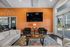 Inviting lounge area with modern decor, featuring a comfortable white sofa, stylish armchairs, and a large wall-mounted TV against a warm orange accent wall.