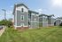Charming apartment complex with modern gray paneling, surrounded by lush green lawns and a sunny, serene atmosphere.