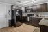 Modern kitchen with sleek dark cabinets, black appliances, and granite countertops, featuring stylish track lighting and wooden flooring.