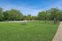 Expansive green dog park with fenced play area and picnic benches under a clear blue sky.