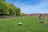 Expansive green dog park with agility features, surrounded by lush trees and scenic apartments in the background.