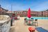 Inviting outdoor space featuring a sparkling swimming pool, stylish lounge chairs, vibrant red umbrellas, and a modern barbecue grill against a backdrop of charming brick apartments.