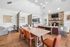 Inviting open-concept living area with a sleek dining table, vibrant orange chairs, and a cozy stone fireplace, perfect for gatherings.