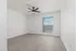 Modern empty room with sleek wood flooring, large window with natural light, and a stylish ceiling fan.