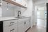 Sleek modern kitchen with white cabinetry, elegant countertop, and stylish black fixtures opening to a bright, airy living space.