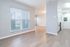 Bright, modern apartment interior showcasing sleek wood-style flooring, large windows with blinds, and a glimpse of the contemporary kitchen.