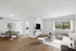 Modern open-plan living room with sleek wooden flooring, featuring a cozy sectional sofa, elegant dining area, and a wall-mounted TV. Sunlit space with large windows and a fresh, inviting ambiance.