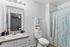 Elegant bathroom with a modern vanity, chic lighting, and tropical-themed shower curtain, featuring a serene view into a cozy bedroom.