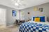 Inviting bedroom with blue and yellow decor, featuring a cozy bed, elegant desk space by the window, and modern wall art.