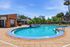 Inviting outdoor pool area with vibrant blue water, surrounded by lush greenery and modern buildings under a clear blue sky.