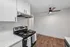 Modern kitchen with sleek white cabinets, stainless steel stove, and stunning wood flooring under a stylish ceiling fan.