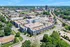 Dynamic aerial view of a modern apartment complex nestled in a verdant urban landscape, showcasing proximity to nearby amenities and lush greenery.