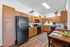 Modern kitchen with sleek black appliances, warm wooden cabinetry, and a cozy dining area, accented by stylish decor and lush greenery.