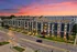Modern apartment building exterior at dusk, showcasing stylish architecture with well-lit windows and a vibrant sunset backdrop.