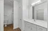 Sleek modern bathroom with white cabinetry, large mirror, elegant lighting, and spacious shower area.