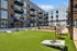 Modern apartment complex featuring stylish balconies overlooking a vibrant outdoor recreation area with lush green lawn and lounge seating.