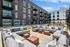 Modern apartment building with expansive outdoor courtyard featuring comfortable lounge seating and vibrant decor, perfect for socializing or relaxing under a clear blue sky.