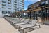 Luxurious apartment complex with modern architecture, featuring a sun-drenched outdoor patio with sleek lounge chairs and a pergola under a clear blue sky.