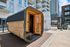 Charming outdoor sauna with a rustic wooden design, set against a modern apartment building backdrop, offering a unique blend of urban and natural relaxation.