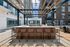 Elegant outdoor terrace featuring a modern pergola, stylish high-top bar seating, and views of sleek urban architecture.