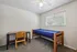 Inviting bedroom with plush carpet, featuring a cozy single bed and a functional study desk, perfect for restful nights and productive days.