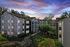 Charming apartment complex with modern architecture, set against a stunning sunset sky, surrounded by lush greenery.