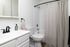 Modern bathroom featuring a sleek white vanity, contemporary fixtures, and a stylish shower-tub combo with a neutral curtain.